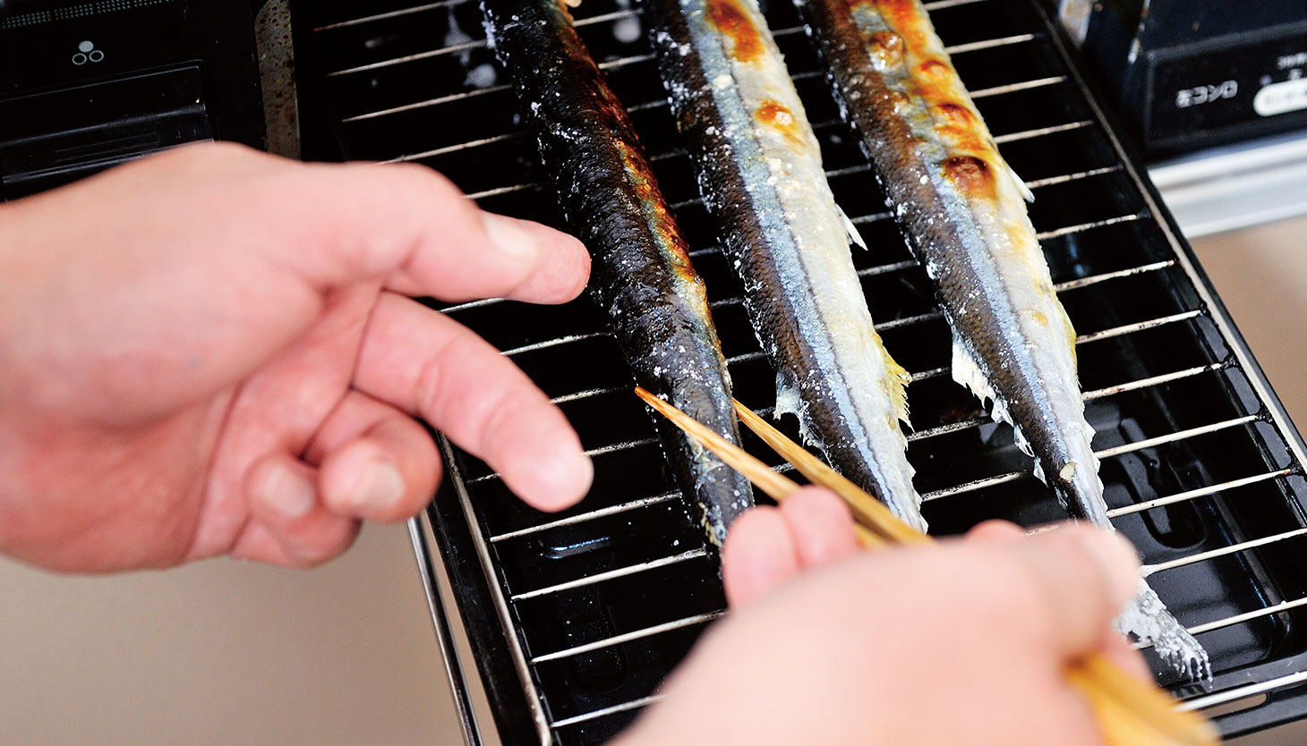 菜箸で焼き加減を確認するさんまの塩焼き