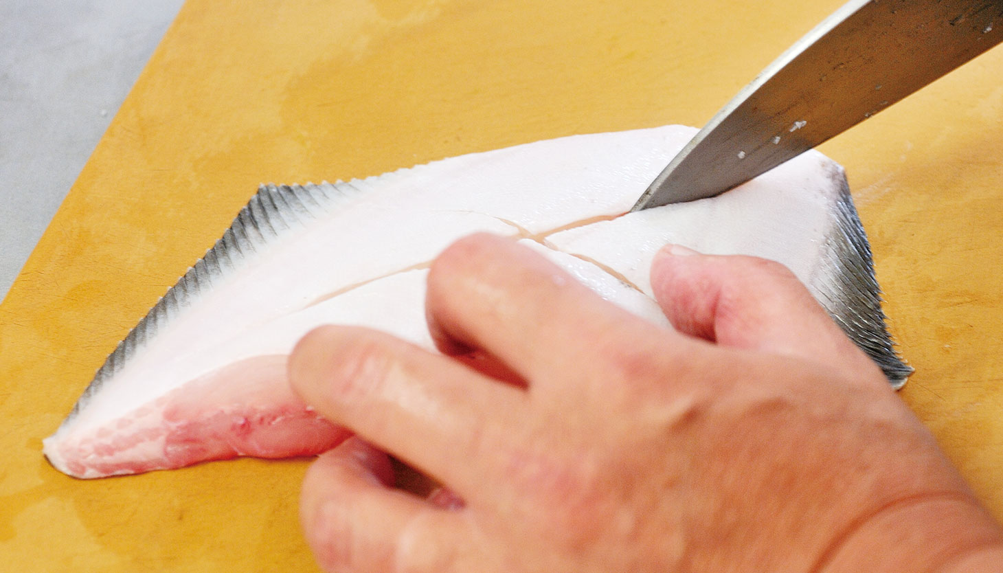 カレイの皮目に包丁で切り込みを入れて下処理している様子