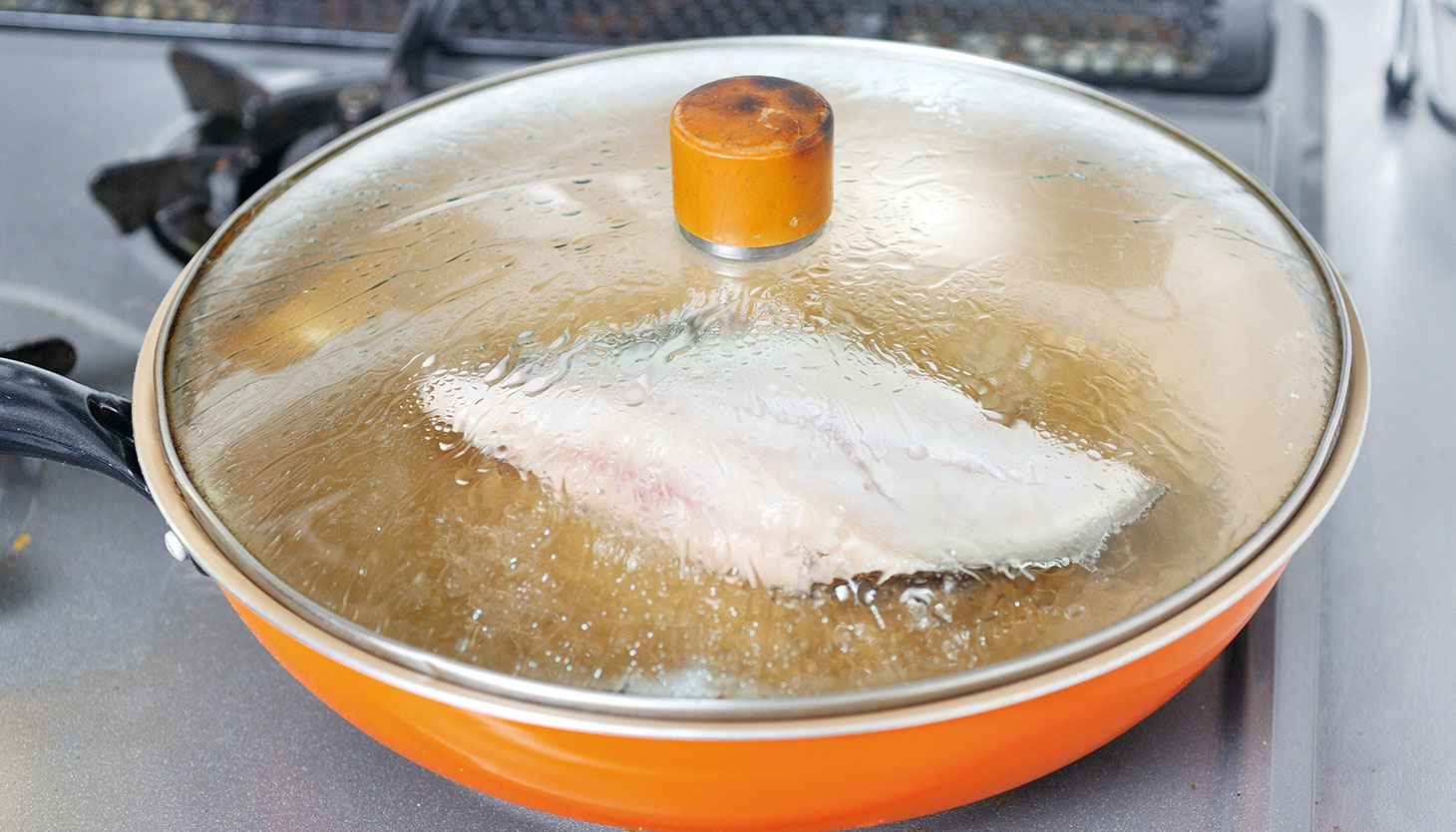 蓋をして酒蒸しにし、カレイに火を通している様子
