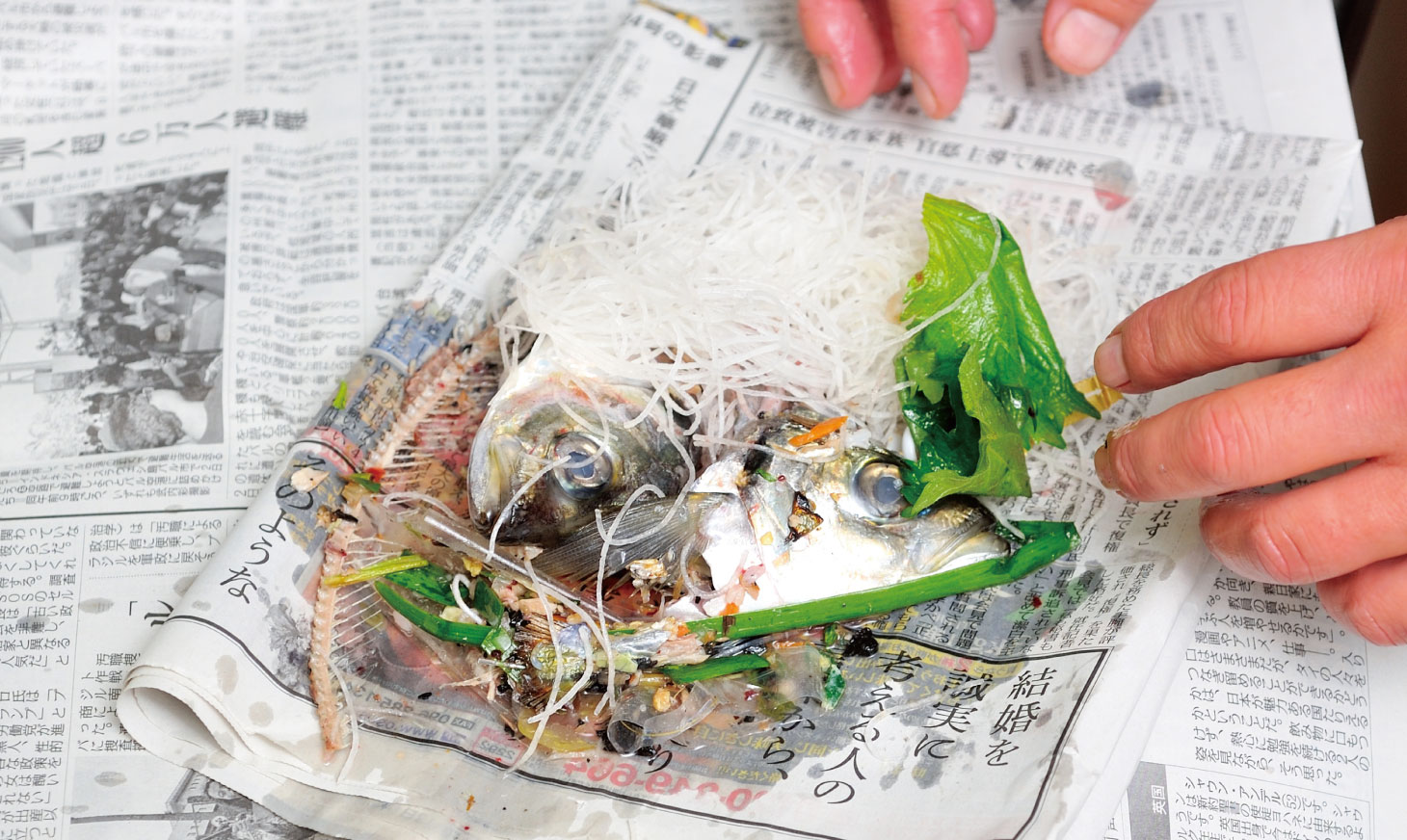 敷いた新聞の上に魚の骨や皮などのゴミを、水を切ってから置くシーン